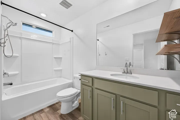 Bathroom featuring a bathtub with an integrated shower, a white toilet, and wood-finish flooring
