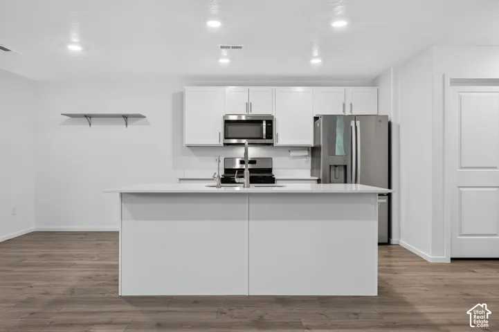 Kitchen featuring white cabinetry, stainless steel appliances, a center island with sink, and wood-finish flooring