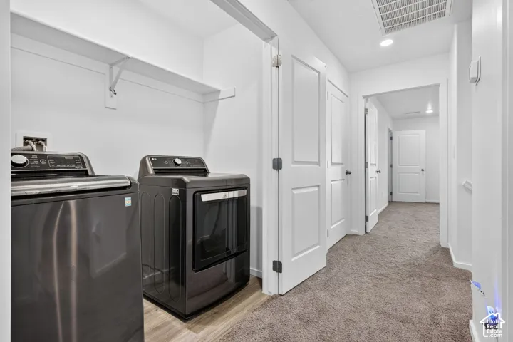 Dedicated laundry area with built-in shelving, wood-finish flooring, and a neutral carpeted hallway with recessed lighting