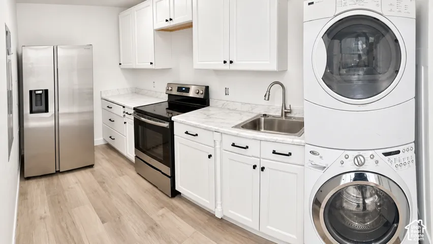 Kitchen featuring white cabinetry, stainless steel appliances, light-toned wood-finish flooring, and a stacked washer/dryer unit