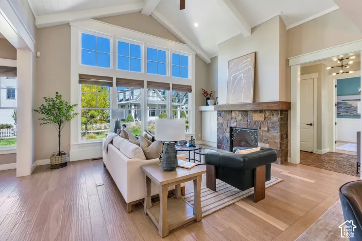 Vaulted ceilings with exposed beams, stone fireplace with wood mantle, light wood-finish flooring, and large picture windows