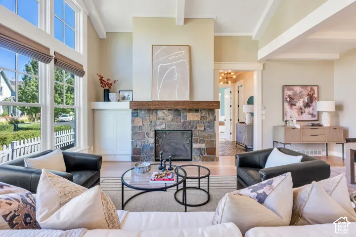Great room featuring a stone-clad fireplace with wood mantel, vaulted ceiling with exposed beams, wood-finish flooring, and large picture windows