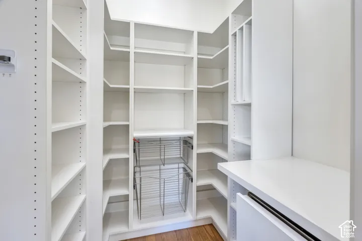 Custom white shelving system with adjustable shelves, integrated wire baskets, built-in drawer, and wood-finish flooring