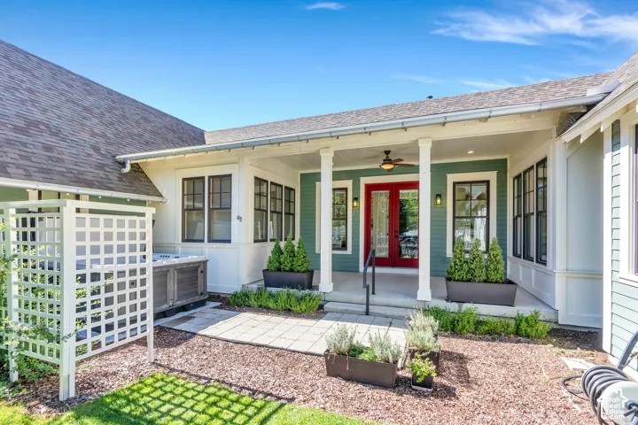 Covered front porch with substantial columns, red double entry doors, exterior lighting, and a ceiling fan