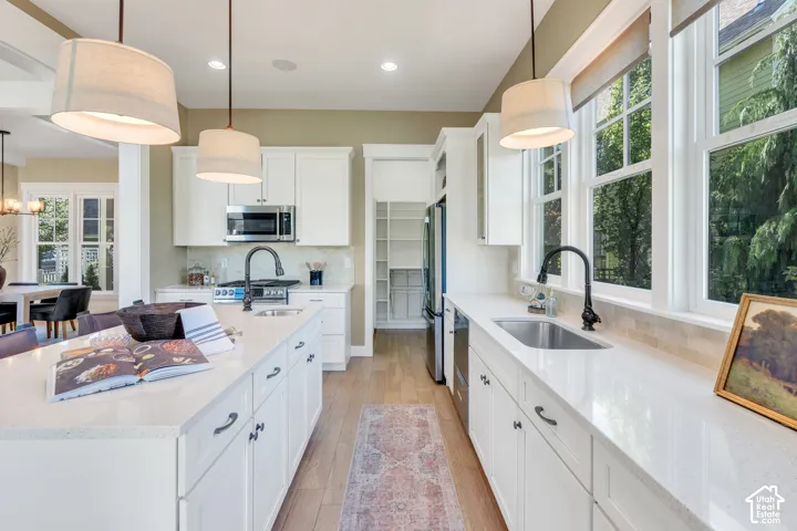 Kitchen featuring a center island, white cabinetry, integrated appliances, wood-finish flooring, and multiple pendant lights