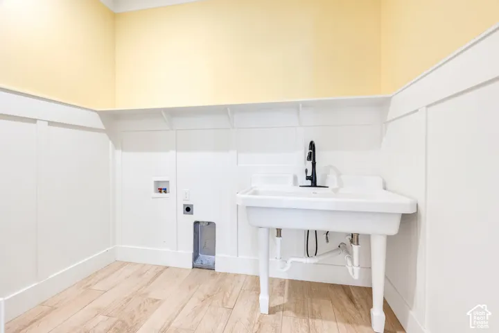 White board and batten wainscoting with an integrated shelf, wood-finish flooring, a white utility sink, and a matte black faucet