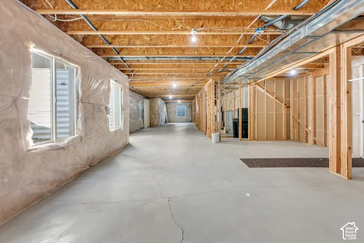 Spacious unfinished basement featuring exposed wood joists, concrete flooring, and multiple windows