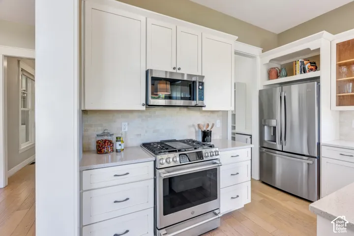 White shaker cabinetry, stainless steel appliances, light-toned wood-finish flooring, light-toned countertops, and a tiled backsplash