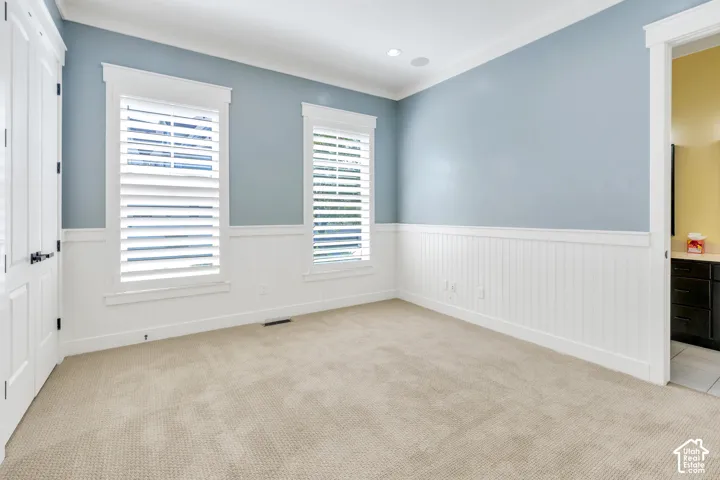 Neutral carpet flooring, white wainscoting, two windows with plantation shutters, recessed lighting, and crown molding