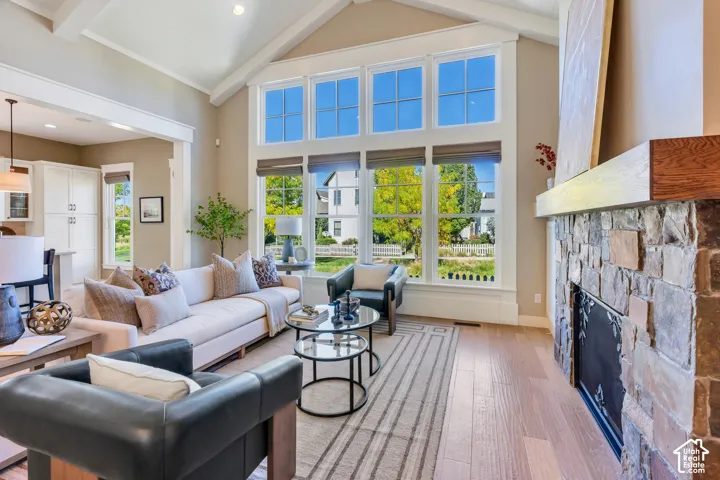 Vaulted ceilings with exposed beams, stone-clad fireplace with wood mantel, large multi-pane windows, wood-finish flooring, and recessed lighting