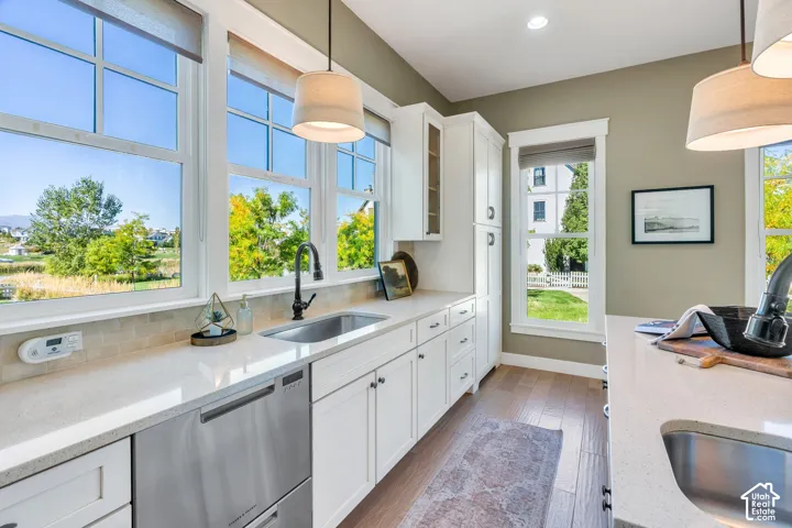 Full-height windows, a stainless steel dishwasher, a single-basin sink with a matte black faucet, white shaker-style cabinetry, and wood-finish flooring