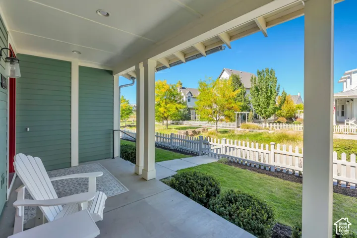 Covered front porch with recessed lighting, shiplap-style siding, and a white picket fence