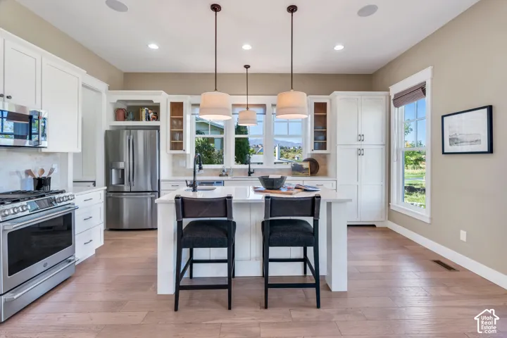 Kitchen featuring white shaker cabinetry, stainless steel appliances, a center island with pendant lighting, wood-finish flooring, and ample natural light