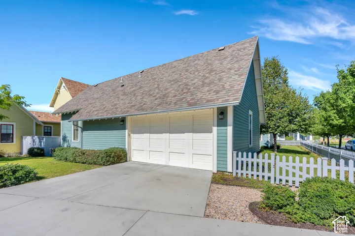 Two-car garage with paneling, asphalt shingle roof, blue siding, concrete driveway, and white picket fence