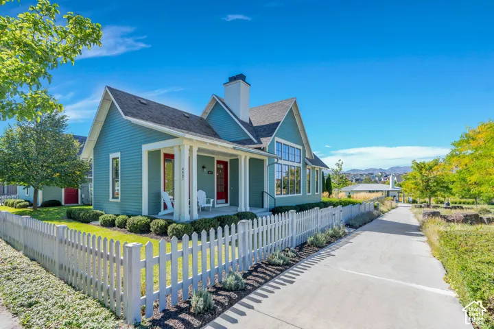 Gable-style home featuring a covered front porch, white picket fence, a large window wall, and a paved pathway