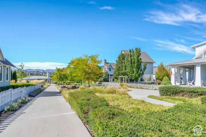Concrete pathway bordered by a white picket fence, mature trees, and landscaped shrubbery