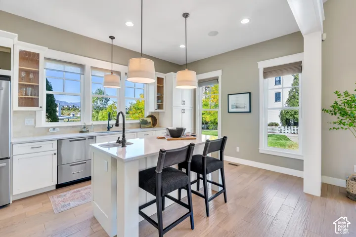 Kitchen featuring a center island with seating, pendant lighting, stainless steel appliances, and wood-finish flooring