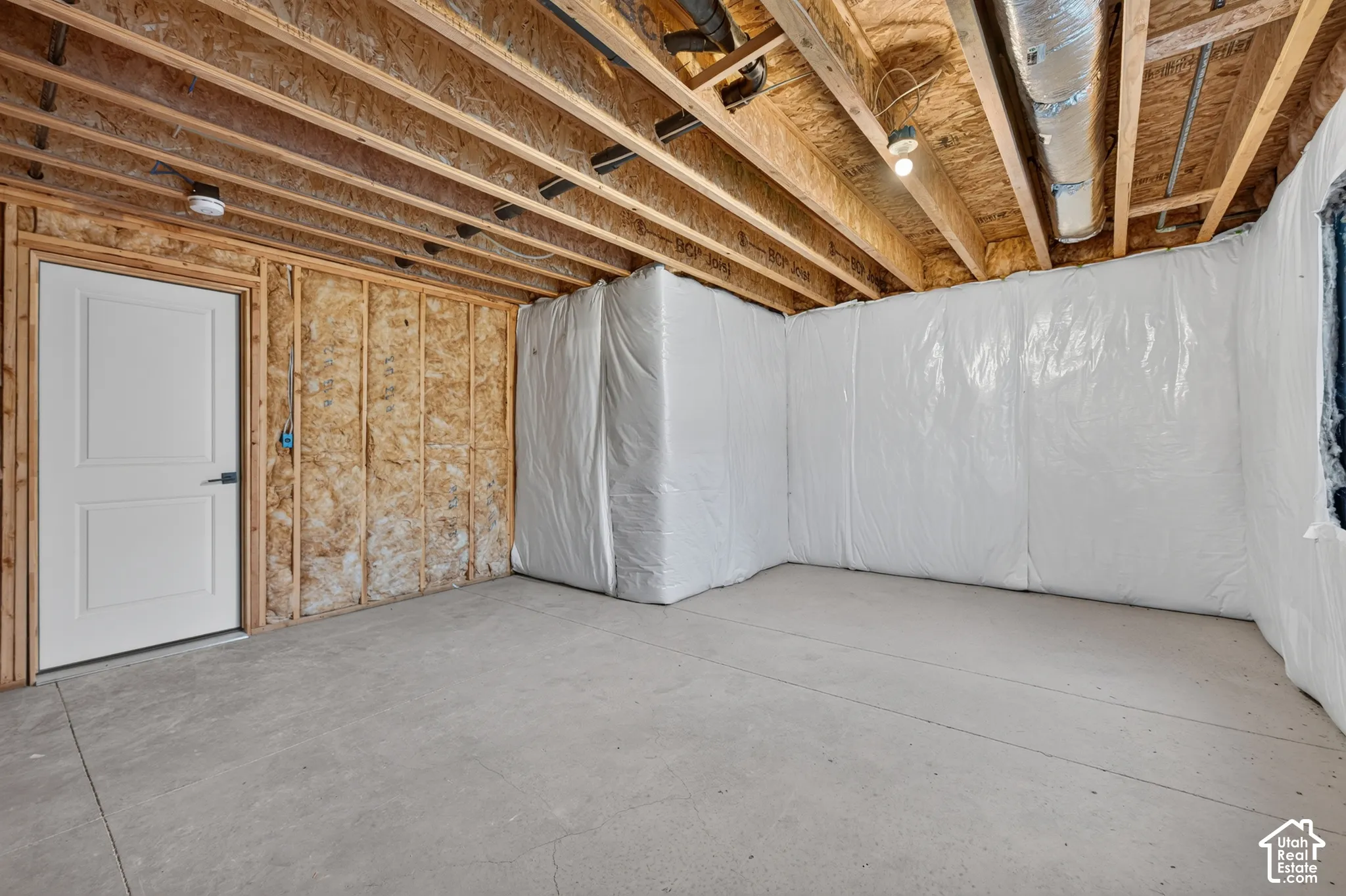 Unfinished basement featuring exposed wood joists, concrete flooring, and a white paneled door