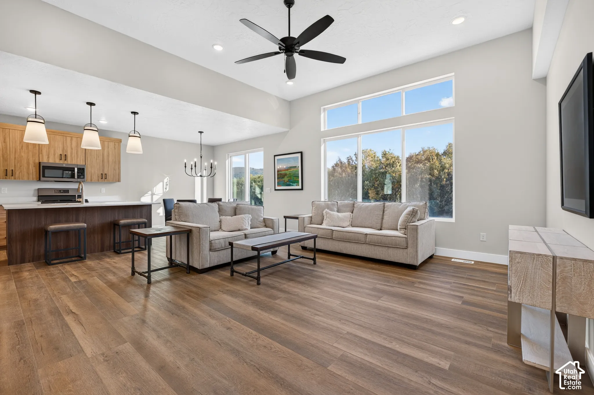 Open-concept living area featuring wood-finish flooring, a large window array, a ceiling fan, and a kitchen with an island and pendant lighting