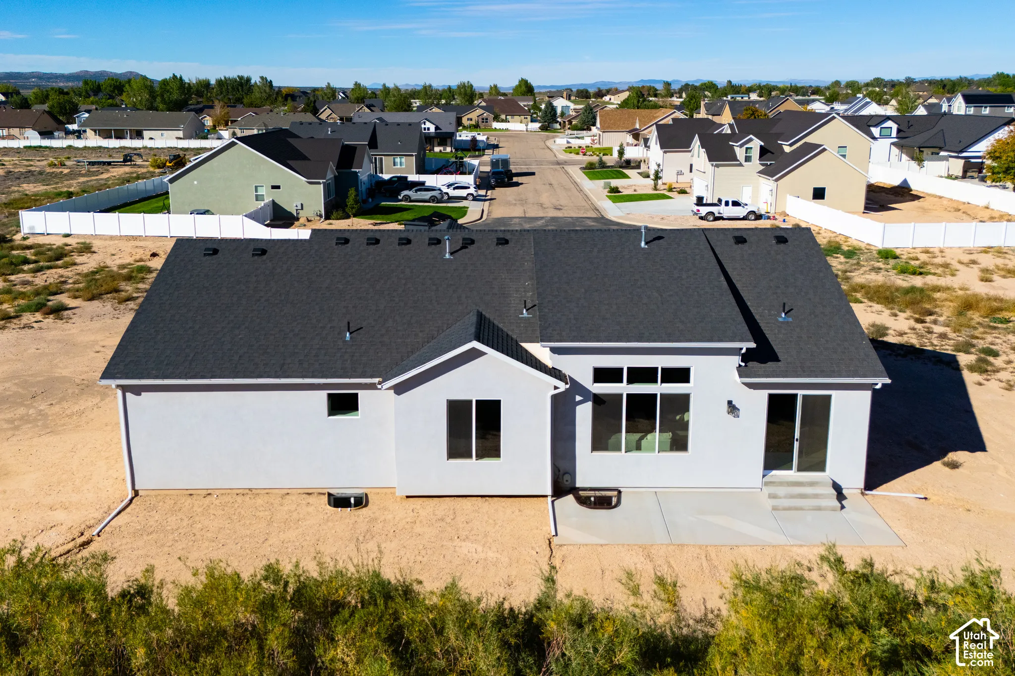 Contemporary exterior with a dark shingle roof, light-colored stucco siding, a concrete patio, and multiple large windows