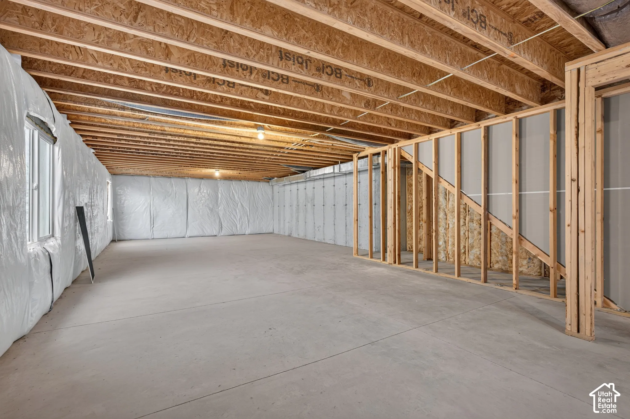 Unfinished basement with exposed ceiling joists, concrete flooring, and framed walls
