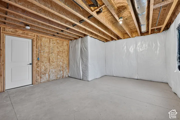 Unfinished basement featuring exposed wood joists, concrete flooring, and a white paneled door