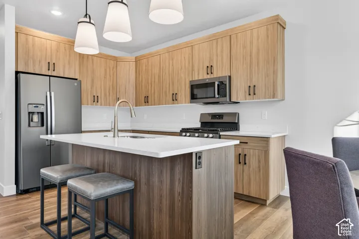 Kitchen featuring wood-finish cabinetry, stainless steel appliances, white countertops, and a central island with a sink