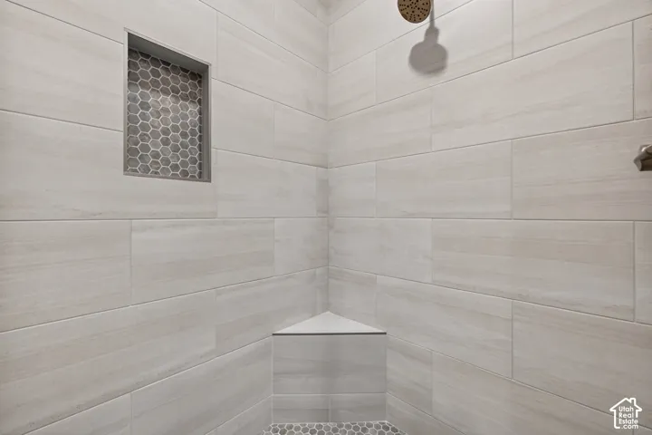 Shower featuring light-toned rectangular wall tiling, a built-in corner bench, a recessed niche with honeycomb mosaic tiling, and a bronze-finish showerhead