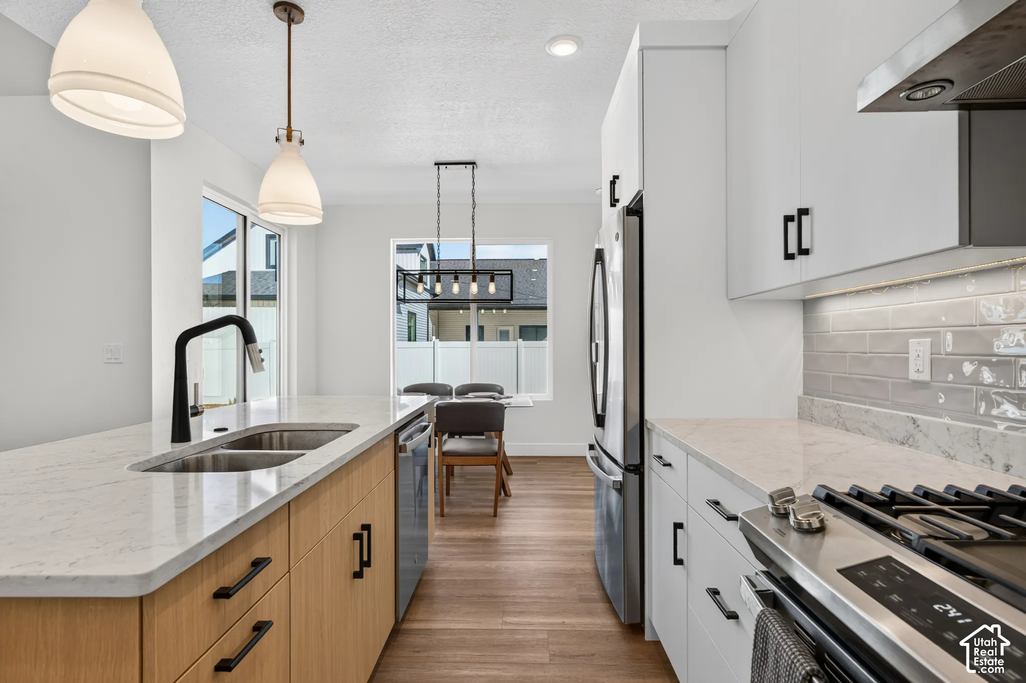 Modern kitchen featuring a dual-tone cabinetry, stainless steel appliances, light-toned countertops, a stainless steel double basin sink, and wood-finish flooring
