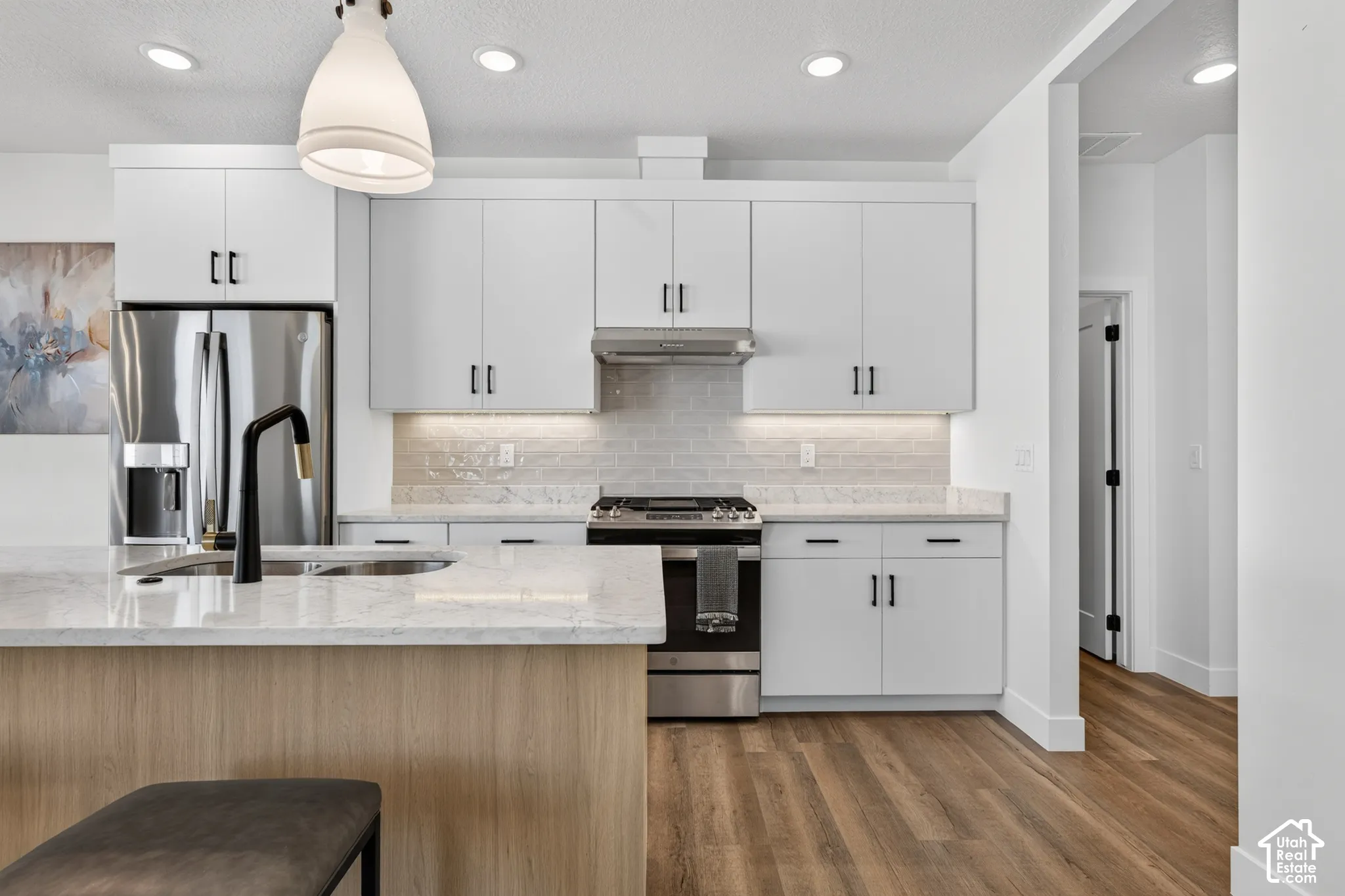 Modern kitchen featuring white cabinetry, stainless steel appliances, a large island with a built-in sink, and wood-finish flooring