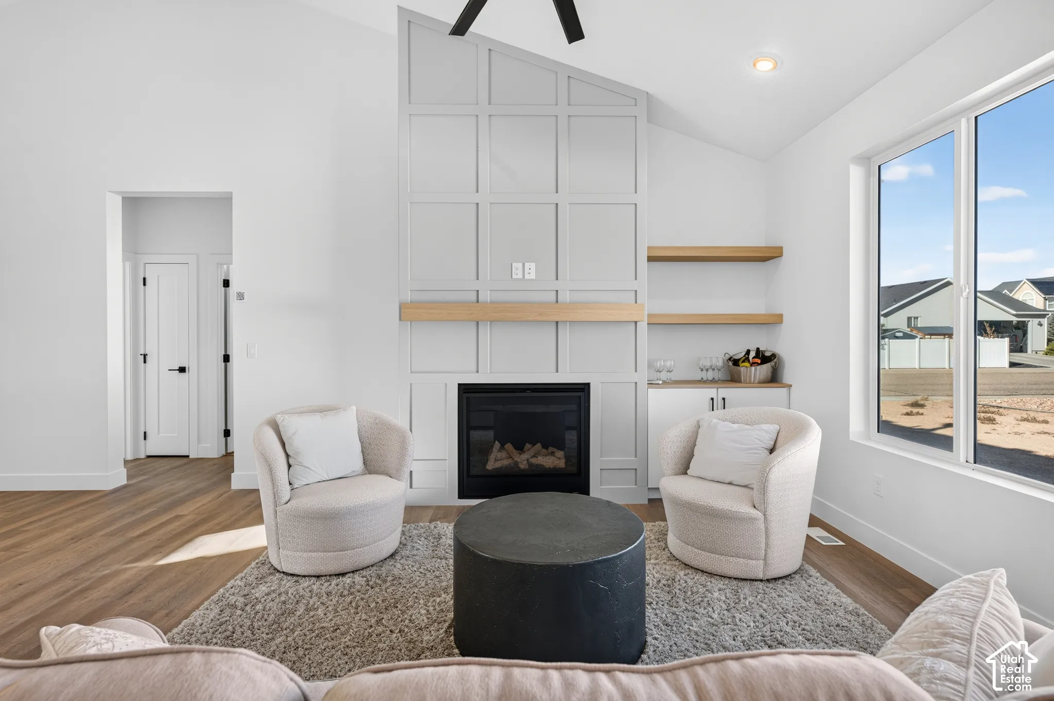 Vaulted ceilings, a built-in fireplace, custom millwork accent wall, wood-finish flooring, and a large window