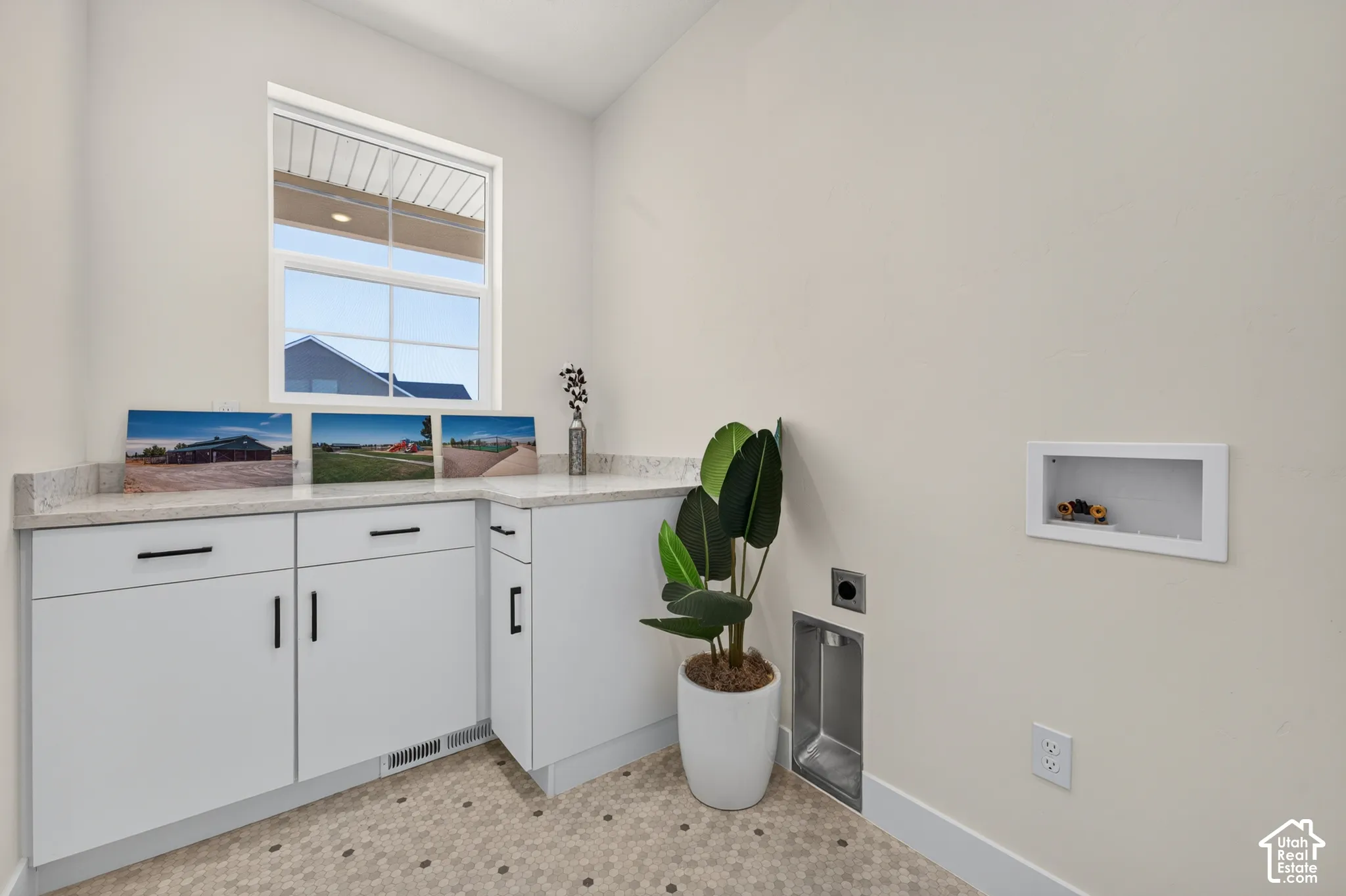 White cabinetry with black hardware, light-toned countertop, hexagon tile flooring, and a single window