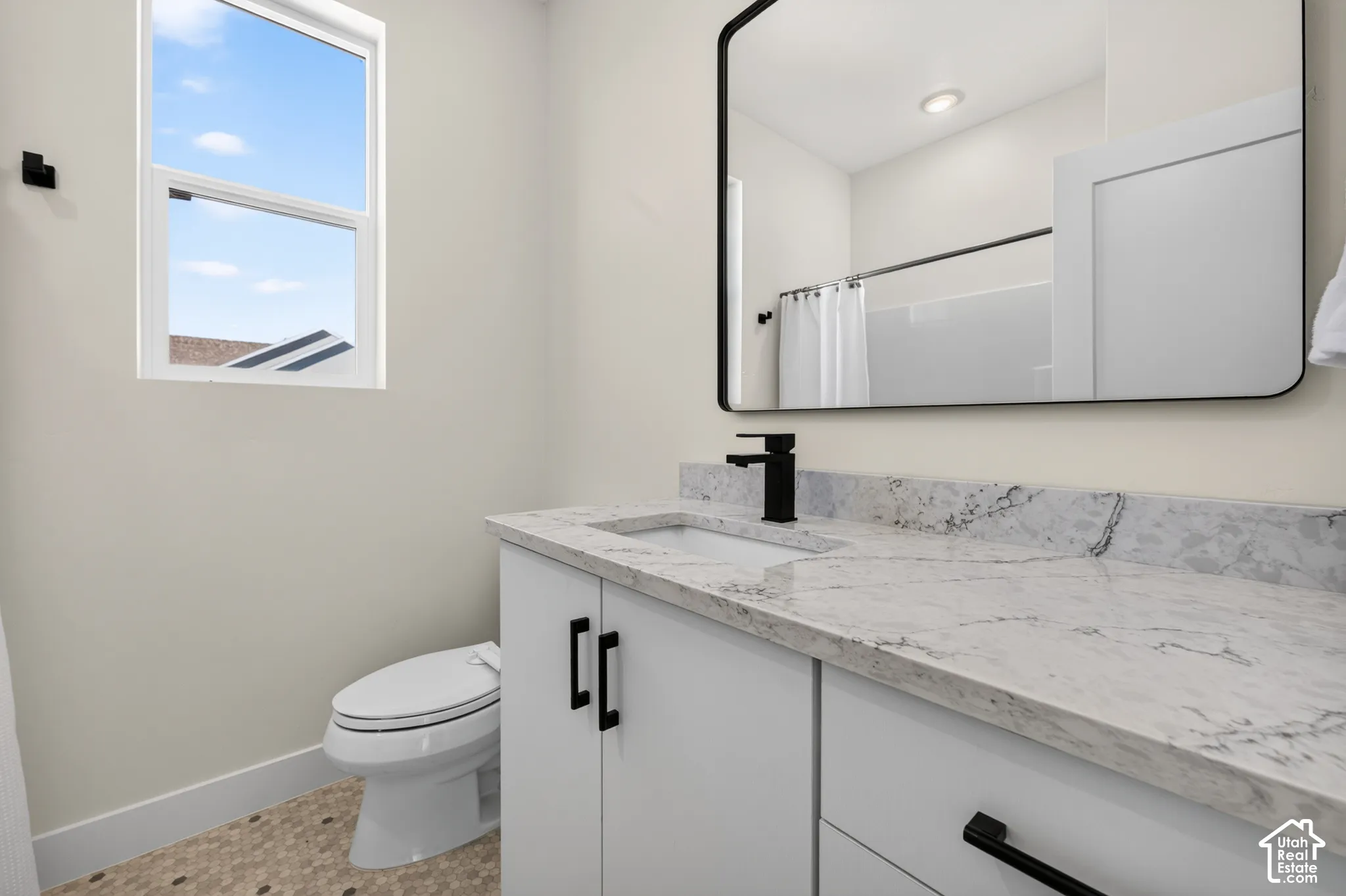 White shaker-style vanity with matte black hardware, stone-finish countertop, and undermount sink
