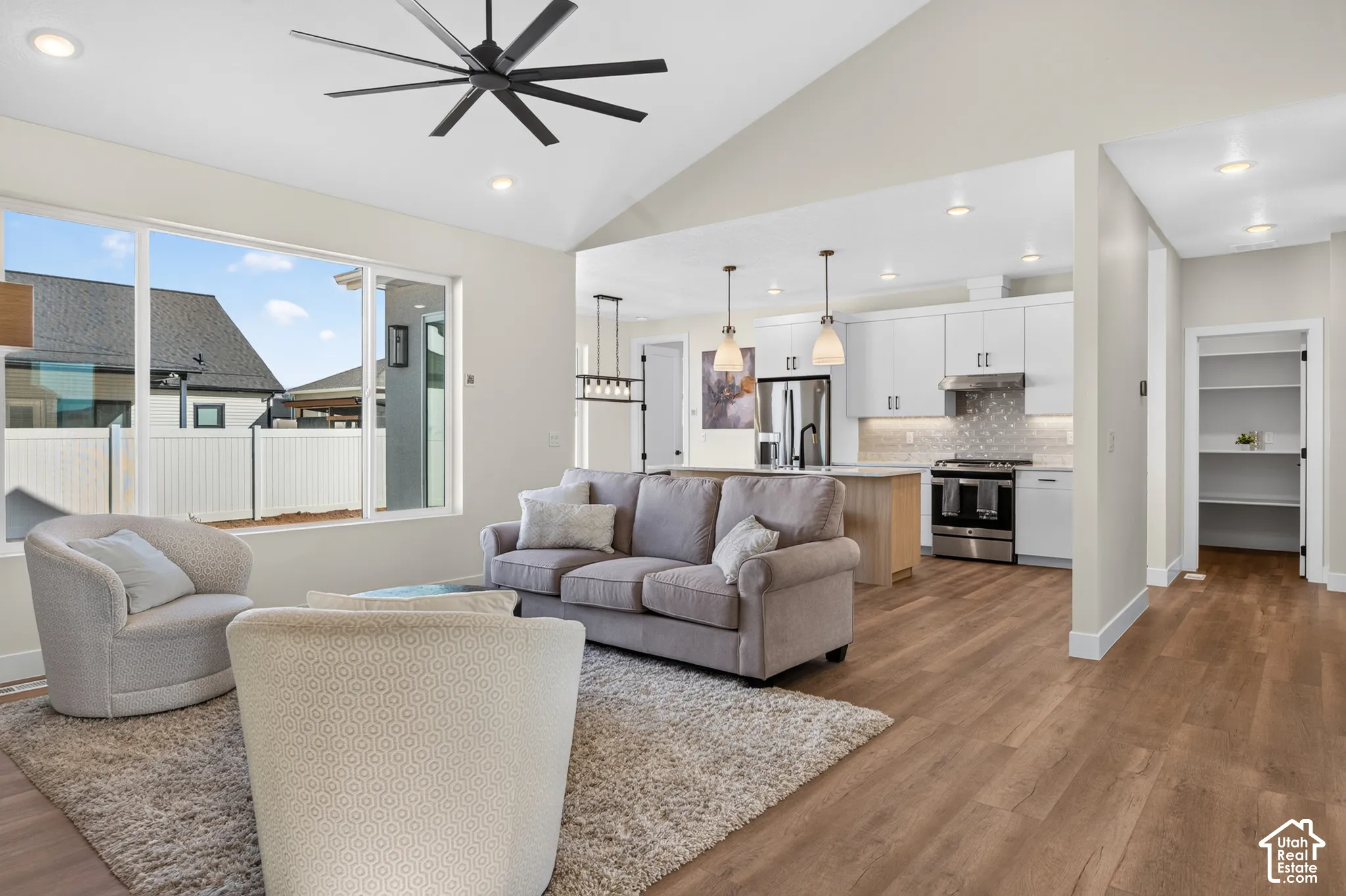 Vaulted ceiling with a black ceiling fan, wood-finish flooring, recessed lighting, and a kitchen featuring a tile backsplash and stainless steel appliances