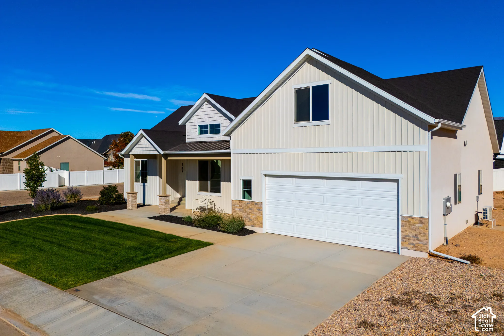 Curb appeal featuring a manicured lawn, an attached garage, a covered entry, and mixed material siding and stone accents