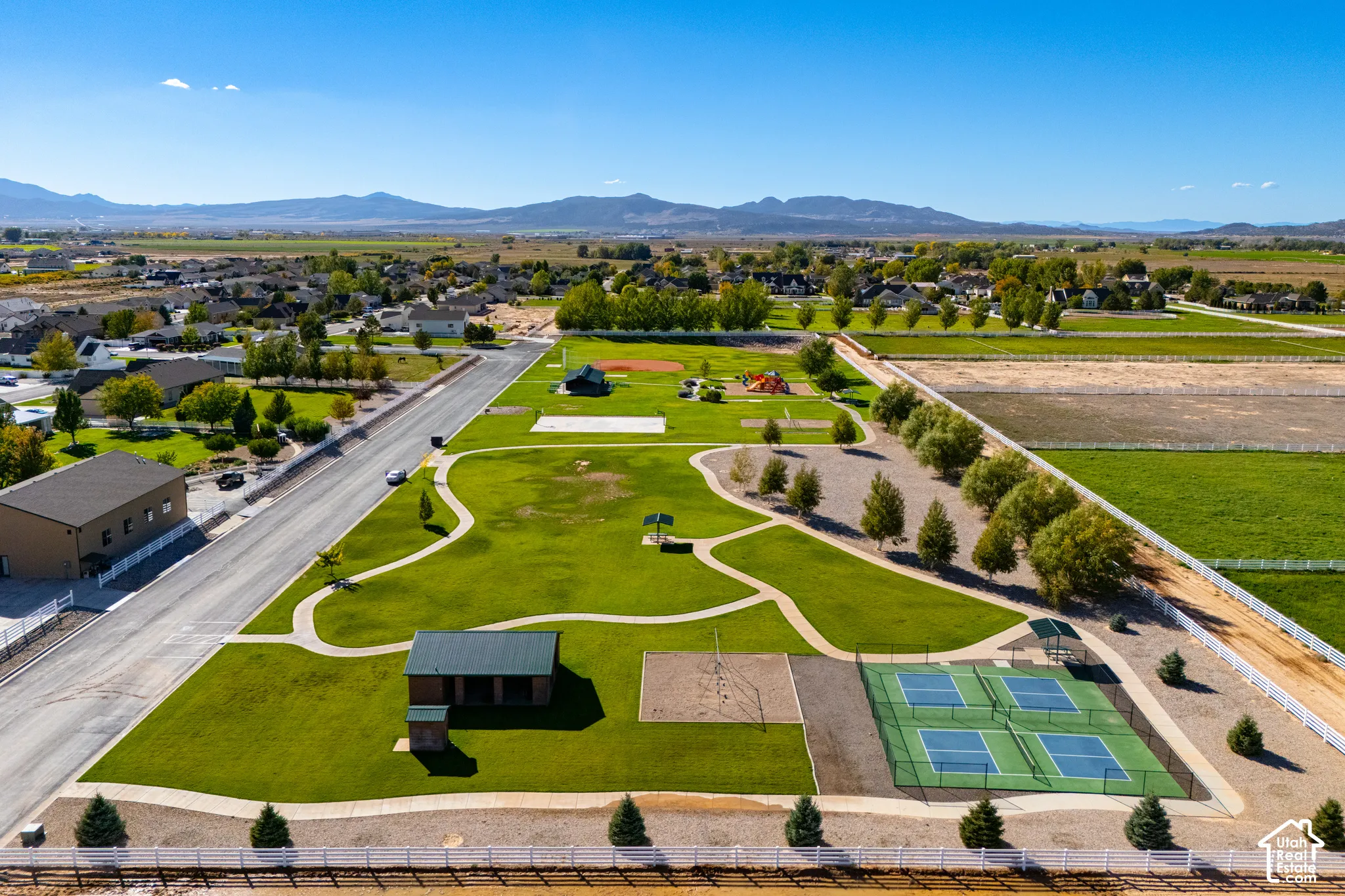 Expansive green space with walking paths, multiple sports courts, a covered pavilion, and distant mountain scenery