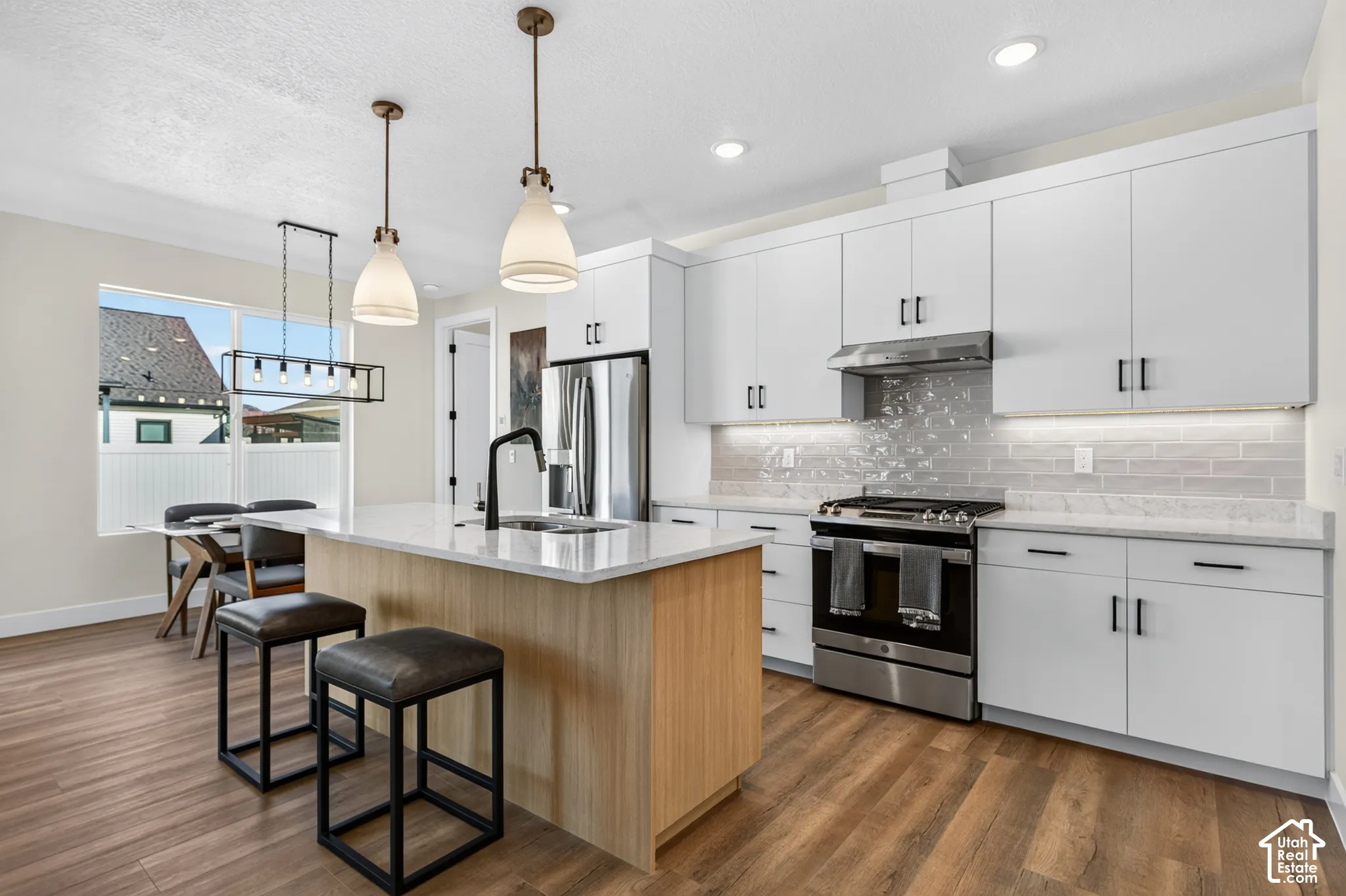 Modern kitchen featuring white cabinetry, light wood-finish flooring, a kitchen island with a light countertop, stainless steel appliances, and pendant lighting