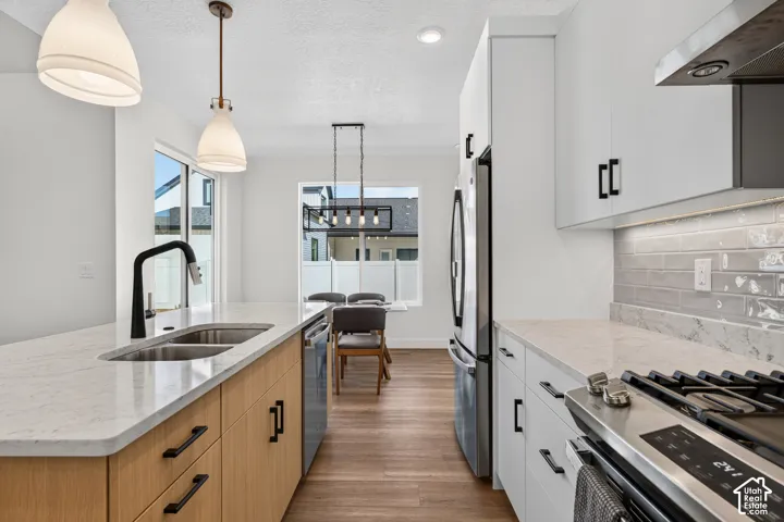 Modern kitchen featuring a dual-tone cabinetry, stainless steel appliances, light-toned countertops, a stainless steel double basin sink, and wood-finish flooring