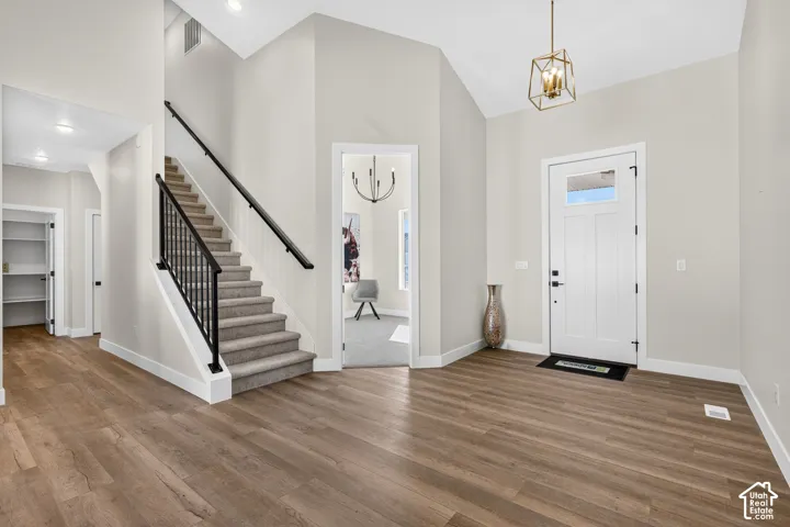Wood-finish flooring throughout, a staircase with black iron balusters, vaulted ceilings, and a geometric pendant light fixture