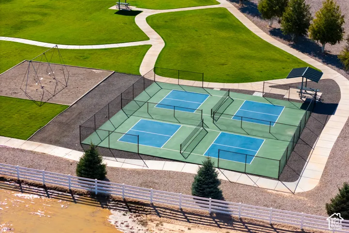 Four pickleball courts, fenced perimeter, adjacent playground structure, covered picnic area, and extensive green space with walking paths