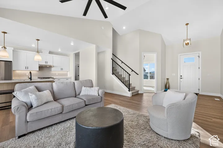 Vaulted ceiling, wood-finish flooring, white kitchen cabinetry, stainless steel appliances, and a built-in staircase with black railing