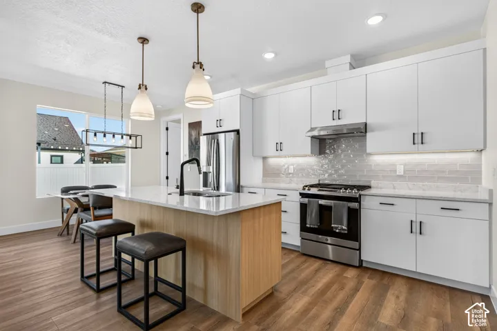 Modern kitchen featuring white cabinetry, light wood-finish flooring, a kitchen island with a light countertop, stainless steel appliances, and pendant lighting