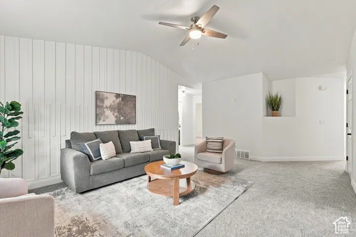 Vaulted ceiling with a ceiling fan, accent wall with vertical paneling, light gray carpeting, and a built-in wall niche