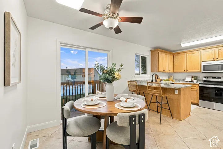 Kitchen and dining area featuring light wood cabinetry, a center island with bar seating, stainless steel appliances, and a sliding glass door