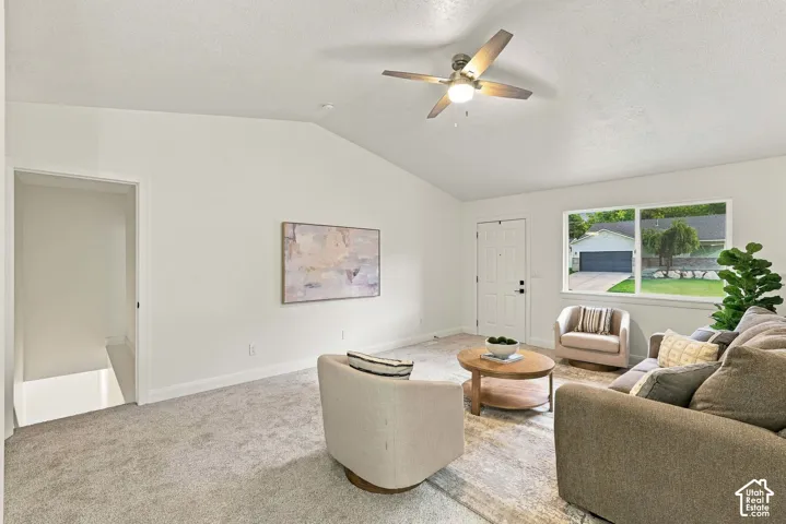 Vaulted ceiling, ceiling fan with light fixture, white interior door, light-colored carpet flooring, and a large window