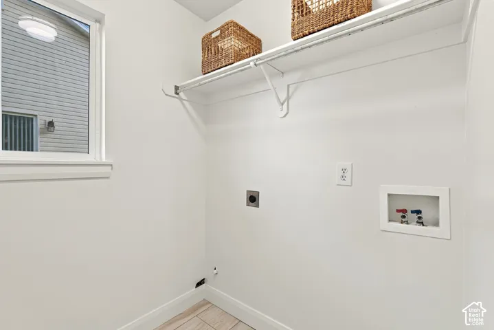 White walls, window with trim, upper shelving with hanging rod, tile flooring, and utility hookups