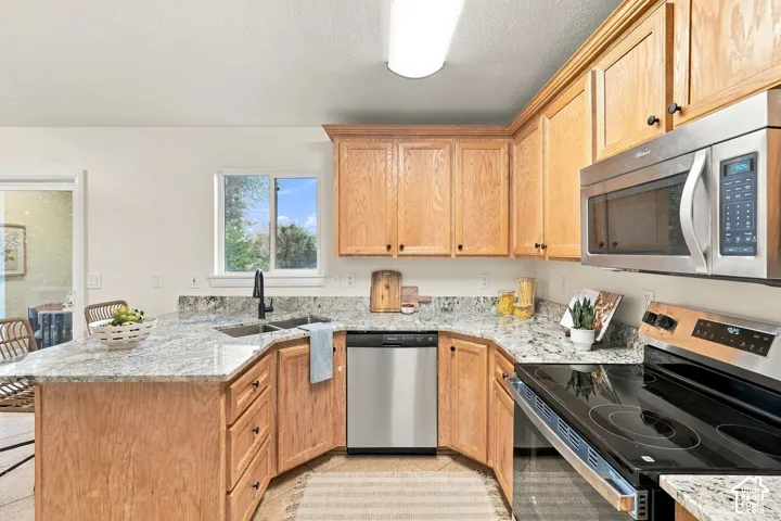 U-shaped kitchen featuring light wood cabinetry, stone countertops, stainless steel appliances, and a window above the sink