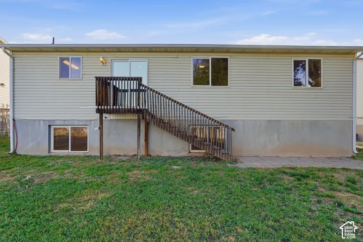 Rear exterior featuring horizontal siding, a wood deck with stairs, sliding glass doors, and a ground-level patio