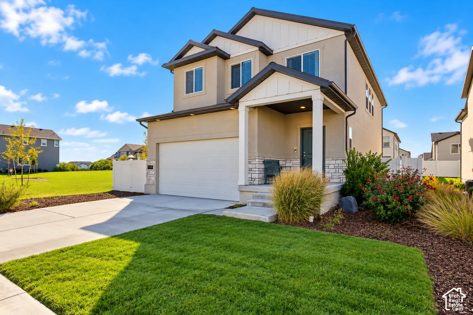 Two-story exterior featuring a mix of stucco and stone veneer siding, covered front porch, dual-gabled roofline, and an attached two-car garage