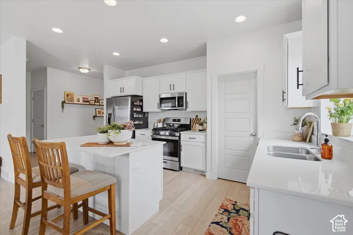 Kitchen featuring white cabinetry with matte black hardware, stone-finish countertops, stainless steel appliances, wood-finish flooring, and a central island